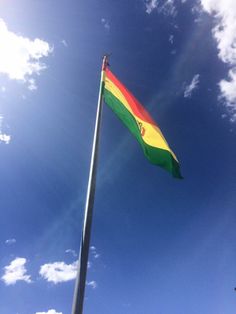 a rainbow colored flag flying high in the sky on a sunny day with blue skies and white clouds