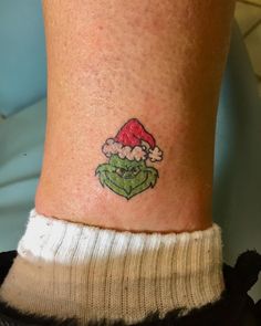 a small tattoo on the ankle of a person wearing a santa hat and green leaves