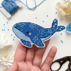 a hand holding a blue whale on top of a table next to scissors and thread