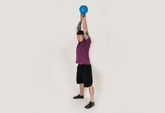 a man holding a blue frisbee above his head while standing in front of a white background