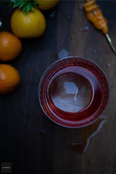 a glass filled with liquid next to oranges and a spoon on a wooden table