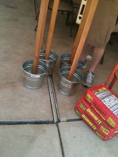 four buckets are sitting on the floor next to a red suitcase and some wooden poles