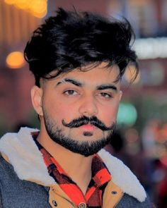 a man with a goatee and a beard wearing a jacket in the city at night