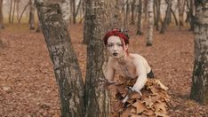 a woman dressed up as a leaf fairy in the woods with leaves on her skirt