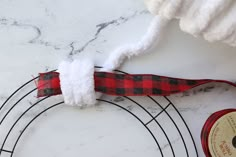 a red and black plaid ribbon is attached to a wire wreath on a marble surface