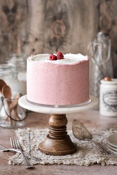 a pink cake with white frosting and raspberries on top sitting on a table