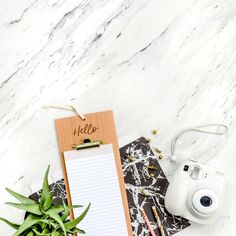 a wooden clipboard with the word hello written on it next to a camera and plant