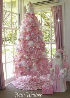 a pink christmas tree decorated with white and pink ornaments is in front of a window