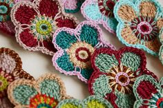 crocheted flowers are arranged in rows on a white tablecloth with red, green, blue, and yellow colors