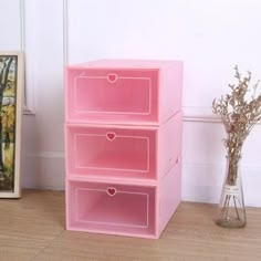 three pink storage boxes sitting on the floor next to a vase with flowers in it