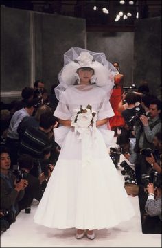 a woman in a white wedding dress and veil walking down the runway at a fashion show