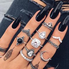 a woman's hand with many different rings on her fingers and black nail polish