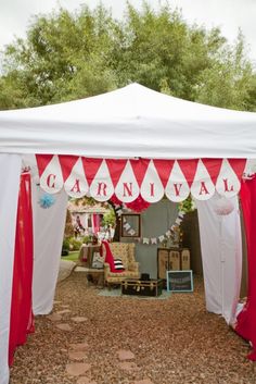 a red and white tent sitting on top of a gravel road next to trees in the background