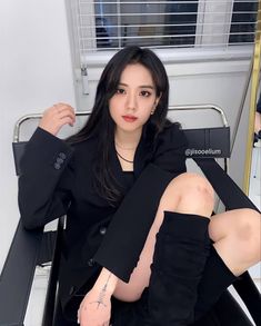 a woman sitting on a chair with her legs crossed and wearing black clothing, posing for the camera