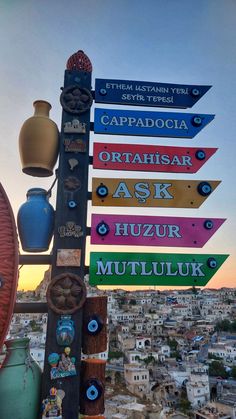 a sign post with many different colored signs on it's side and buildings in the background