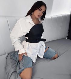 a woman sitting on top of a gray couch next to a white wall and wearing jeans