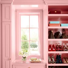 a pink closet filled with lots of shoes and purses next to a white table