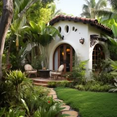 a white house surrounded by greenery and palm trees in the daytime with an outdoor seating area