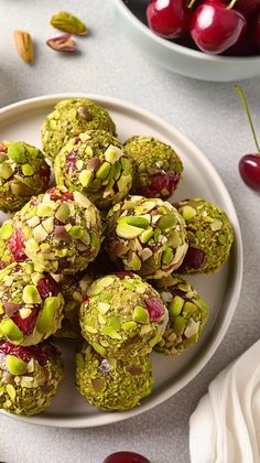 a white plate topped with cookies covered in nuts and cherries next to a bowl of cherries