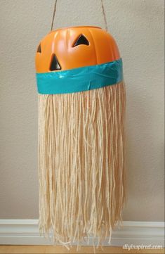 an orange pumpkin hanging from a string with fringes on it's head and eyes