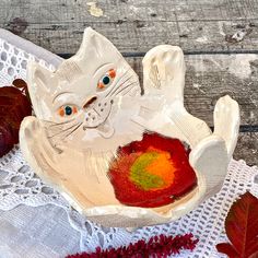 a white cat sitting in a bowl on top of a doily covered table cloth