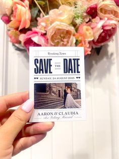 a person holding up a save the date card next to a bouquet of pink and yellow flowers