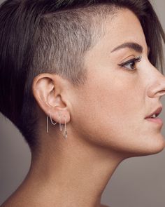 a close up of a person with short hair and piercings on her ear wearing earrings