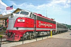 a red and silver train traveling down tracks next to a flag on top of a building