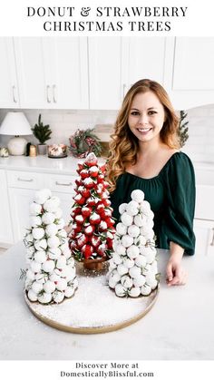 a woman standing in front of a christmas tree on top of a kitchen counter with white cabinets