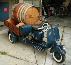 an old blue motorcycle parked next to a wooden barrel on the back of a scooter