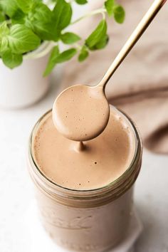 a spoon full of peanut butter on top of a jar with basil in the background