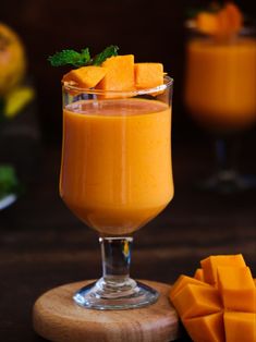 an orange smoothie in a glass next to sliced mangoes and pieces of parsley