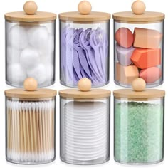 four clear canisters with wooden lids filled with different types of beads and other items