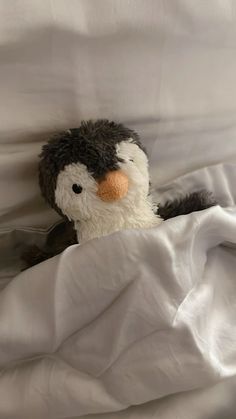 a stuffed penguin is peeking out from under the covers on a white sheeted bed