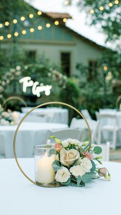 a white table topped with a vase filled with flowers next to a lit candle on top of a table