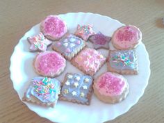 a white plate topped with cookies covered in frosting and sprinkles on top of a wooden table