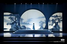 a person standing on a stage in front of an artistic backdrop with trees and mountains