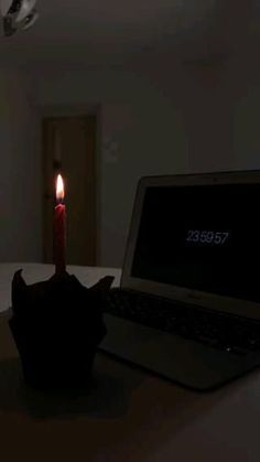 a laptop computer sitting on top of a table next to a lit candle in the dark