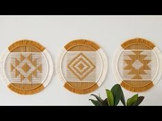 three woven wall hangings with geometric designs on the sides and one has a potted plant in front of it