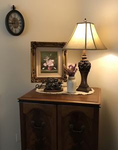 a table with a lamp and some pictures on top of it next to a wall clock