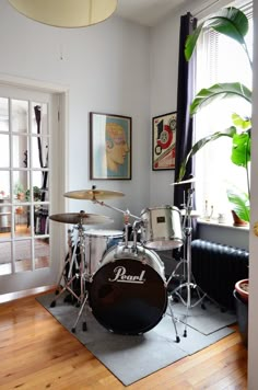 a drum kit is sitting on the floor in front of a window with potted plants