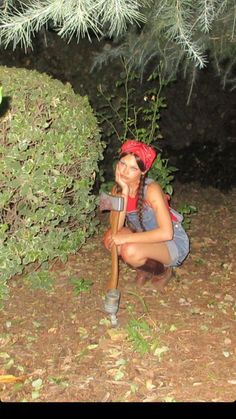 a woman kneeling down in the dirt with a pickle on her hand and a tree behind her