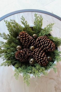 pine cones and evergreen needles in a white bowl on a marble table with silver bells