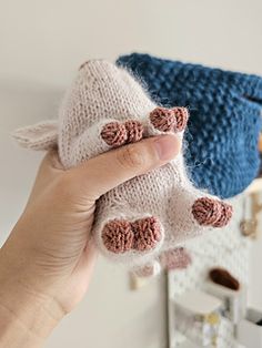 a hand holding a small stuffed animal in front of a blue bag on the wall