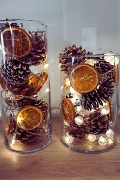 two glass vases filled with orange slices and pine cones