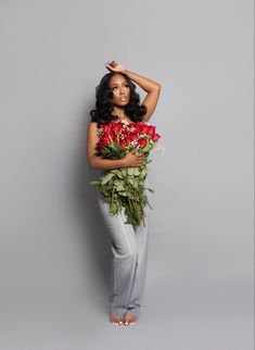 a woman holding flowers in her hands and posing for the camera on a gray background