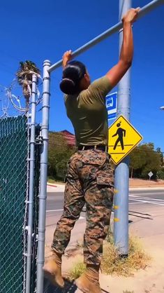 a man in camo pants is hanging on a fence with a baseball cap over his head