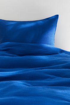 a bed with blue sheets and pillows on top of it, against a white wall