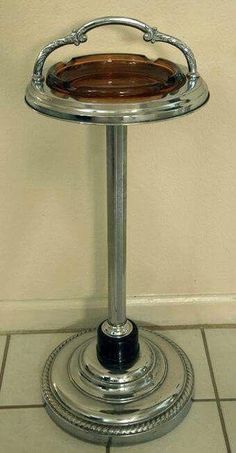 a silver pedestal with a wooden tray on it's top sitting in front of a wall