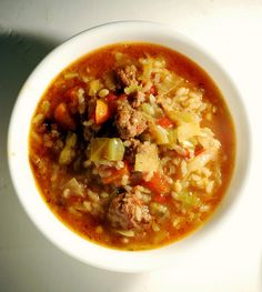 a white bowl filled with meat and vegetable soup on top of a table next to a spoon